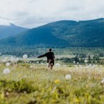 a man is walking through a field with mountains in the background